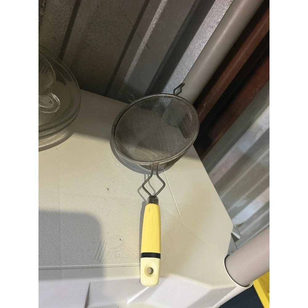 The vintage Eckoline hand-held mesh strainer with a yellow and white plastic